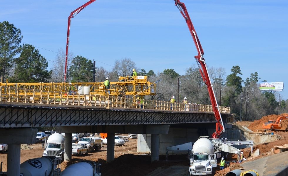 Concrete being poured onto a bridge deck using pump trucks while workers install formwork
