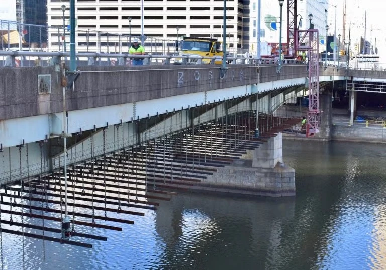Bridge construction work over a river, showing steel support beams installed beneath the bridge deck 