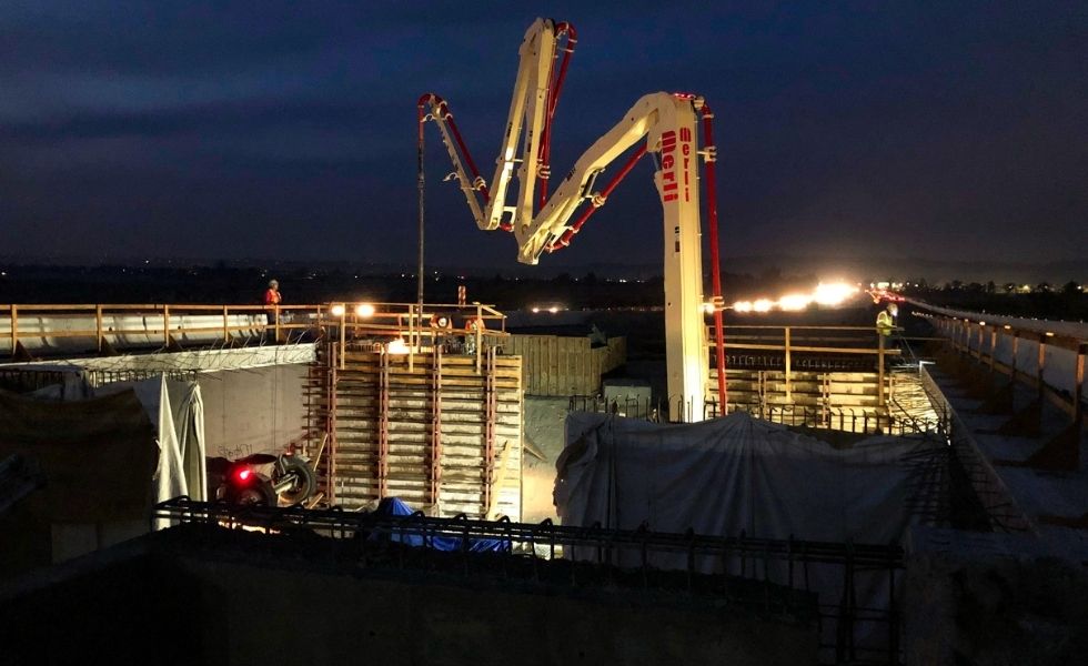 Nighttime construction scene showing concrete pumping operations on a bridge structure