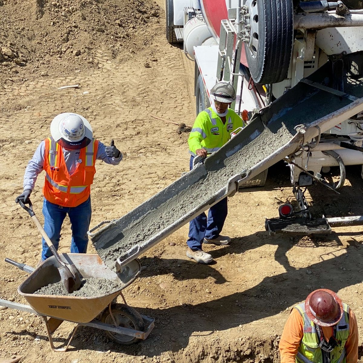 Close-up view of workers collecting fresh concrete from a truck chute into a wheelbarrow at a construction site