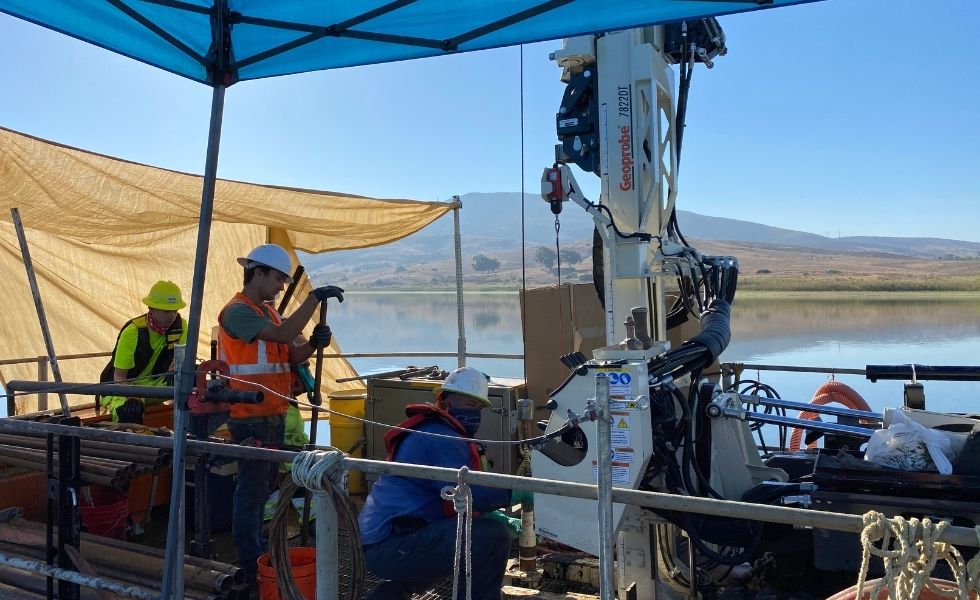Multiple technicians operating drilling equipment on a floating platform over a reservoir