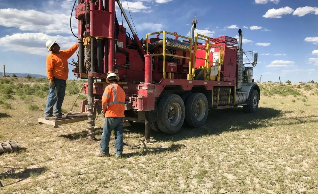 A drilling truck with an attached auger creating holes in the ground at an open field