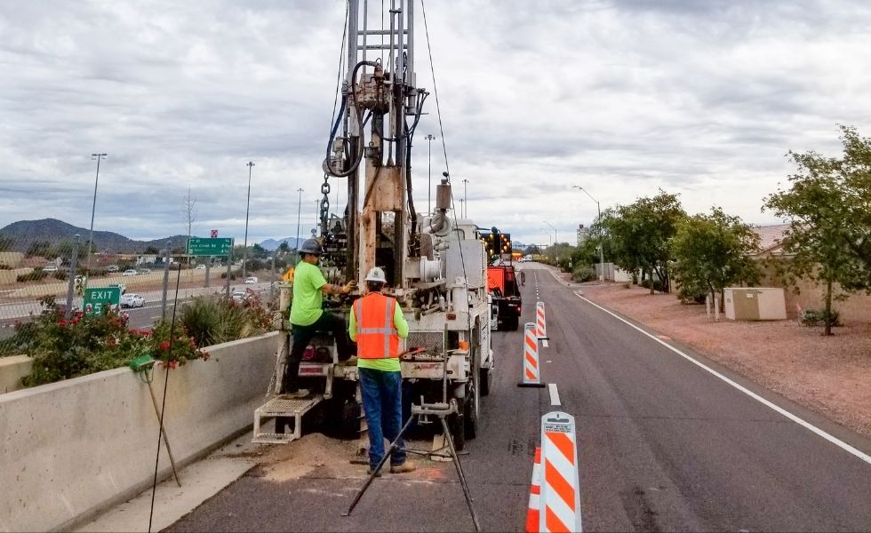 Geotechnical drilling rig operating on a roadside shoulder next to an active freeway