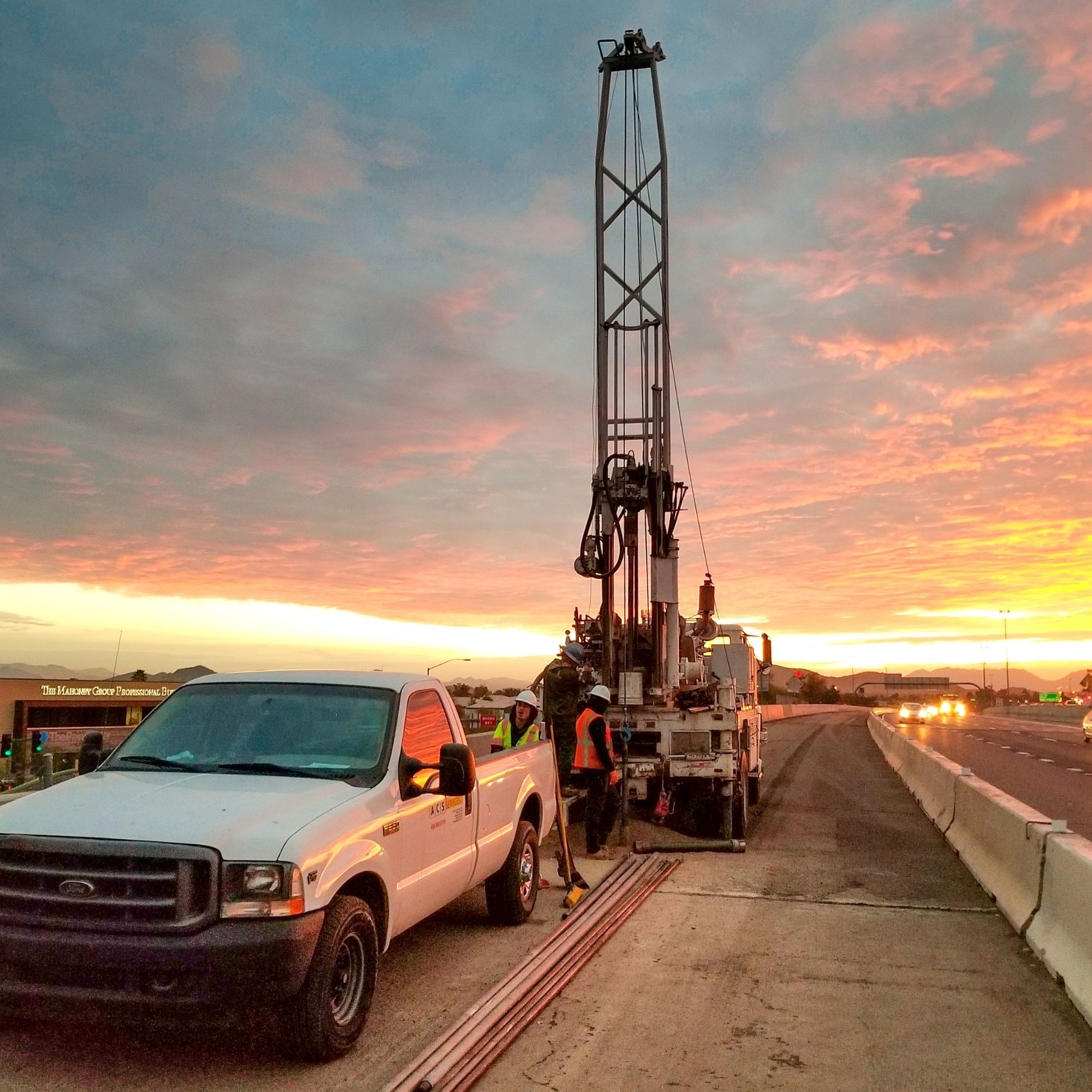 Track-mounted geotechnical drilling rig operating on a highway shoulder at sunrise