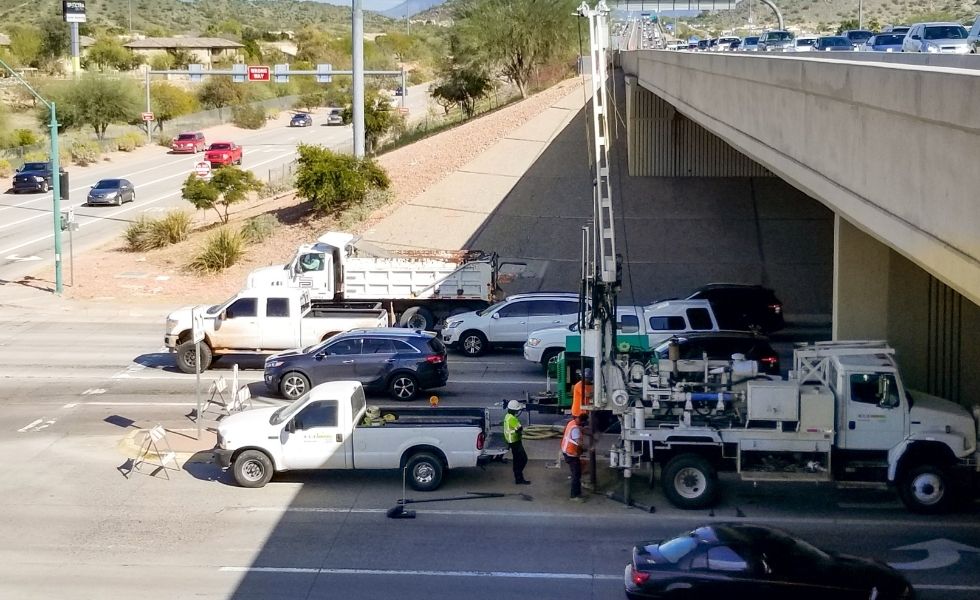 Truck-mounted geotechnical drilling rig operating beneath a highway overpass at a busy intersection