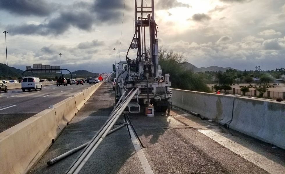 Drilling rig positioned along a divided highway with traffic passing in adjacent lanes