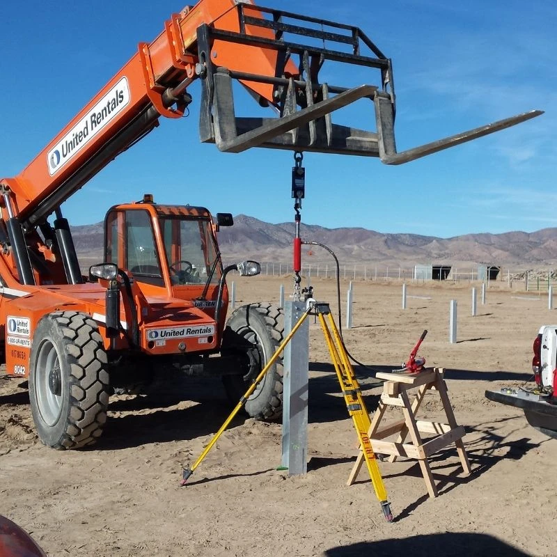 A telescopic forklift lifting equipment near metal posts in a desert construction site