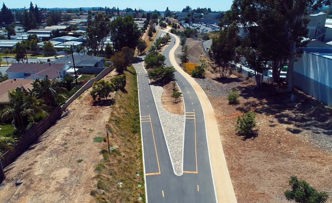 Aerial view of a landscaped urban corridor featuring two parallel paved bike lanes separated by a rock-lined median
