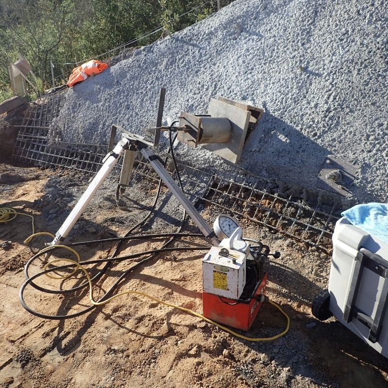 Rebuilding Community Infrastructure - Field technician conducting quality testing on a shotcrete slope stabilization wall