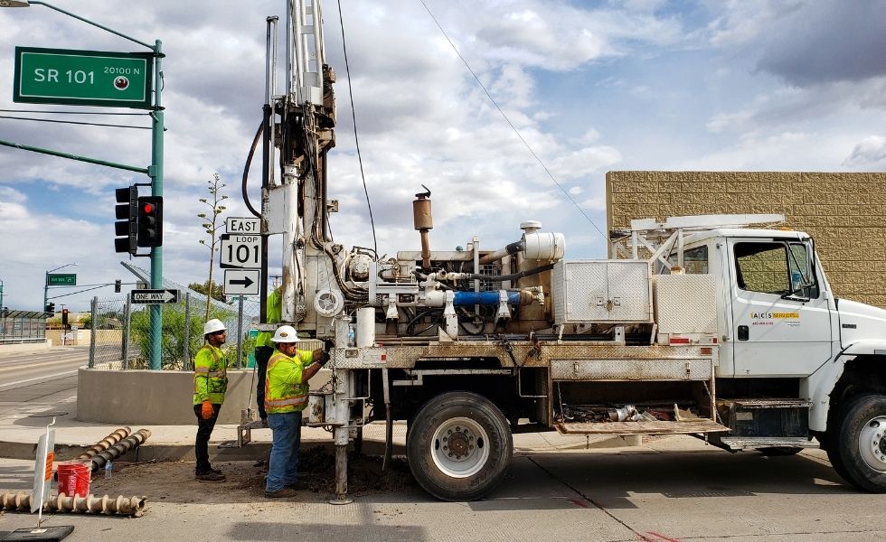 Geotechnical drilling truck and crew working along a roadway near SR 101 signage