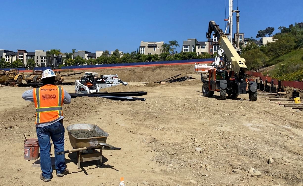 Construction crew coordinating concrete placement for shoring caissons using a concrete truck chute