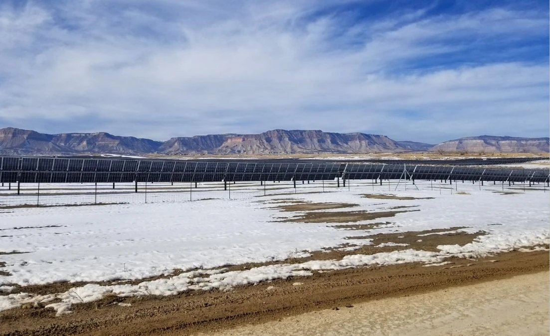 Rows of solar panels installed in a large field partially covered with snow