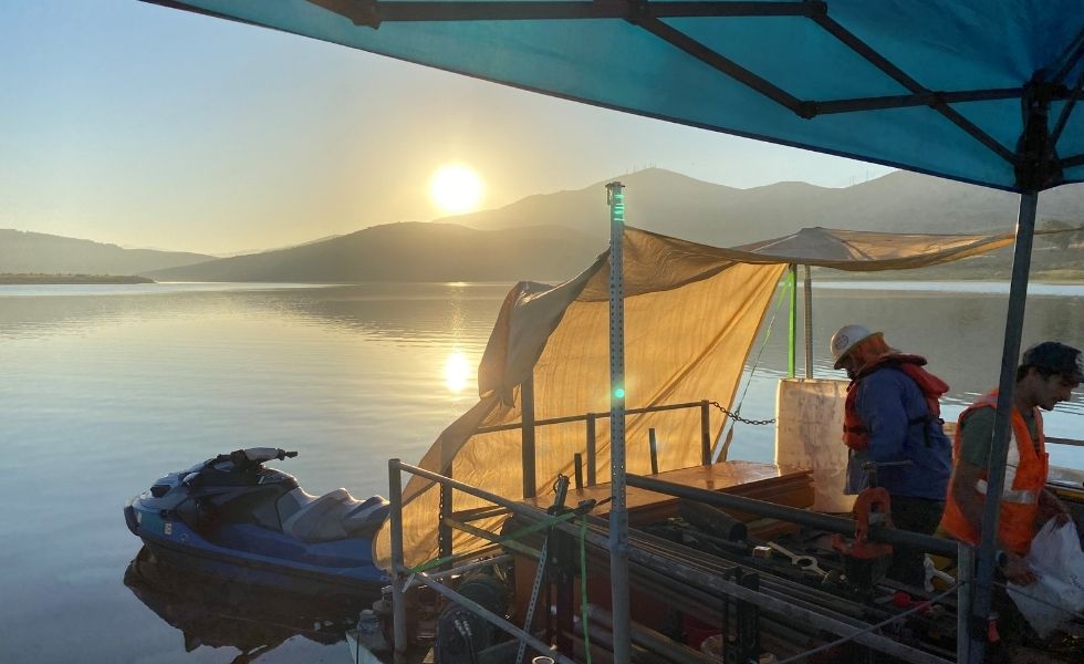 Field team working from a floating platform on a calm reservoir during sunrise