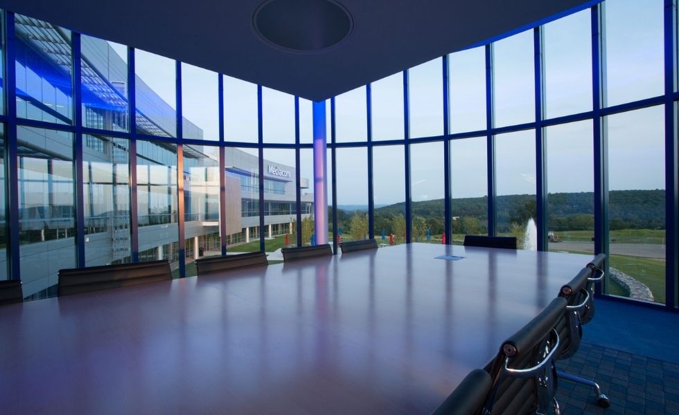 Interior view of a conference room at the Mediacom Corporate Headquarters in New York featuring a large boardroom table, modern seating, and floor-to-ceiling curved glass walls.