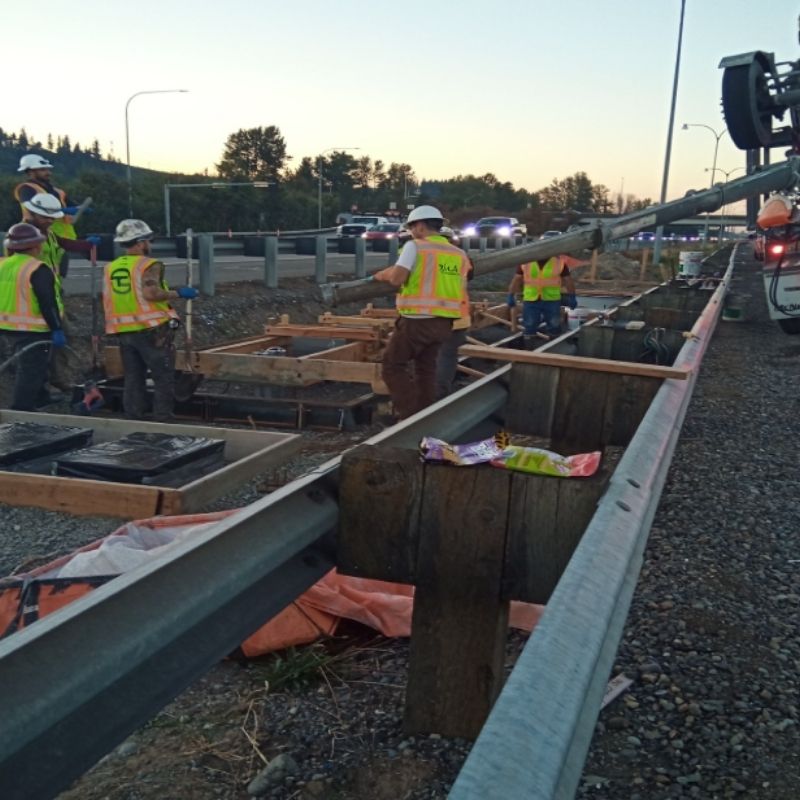 Construction workers install a concrete drainage structure adjacent to the SR 167 highway as part of the SR 167 Corridor Improvements Project.