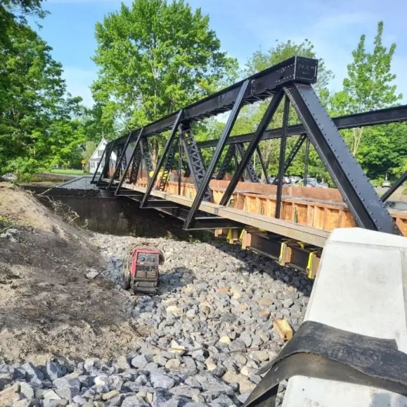 Steel truss bridge under construction for the Howellville Road Bridge project, showing the newly installed bridge structure spanning a rock-lined channel with riprap stabilization