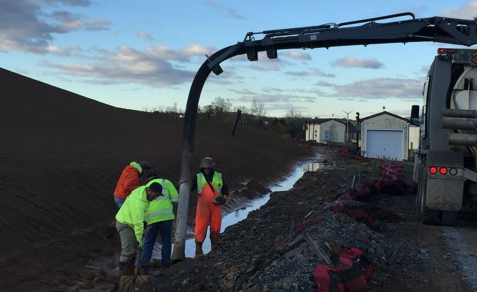 Construction workers installing stormwater drainage components in an excavated channel beside a construction access road at the PhilaPort Auto Storage Facility.