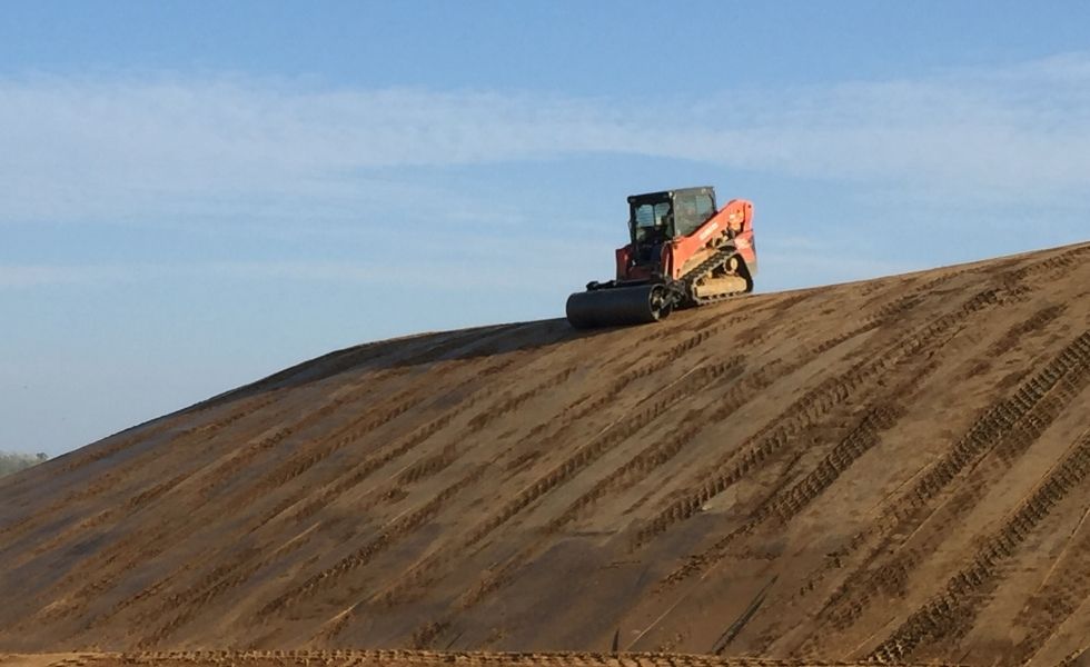 Compact track loader operating on a large earthen slope during grading and compaction activities at the PhilaPort Auto Storage Facility.