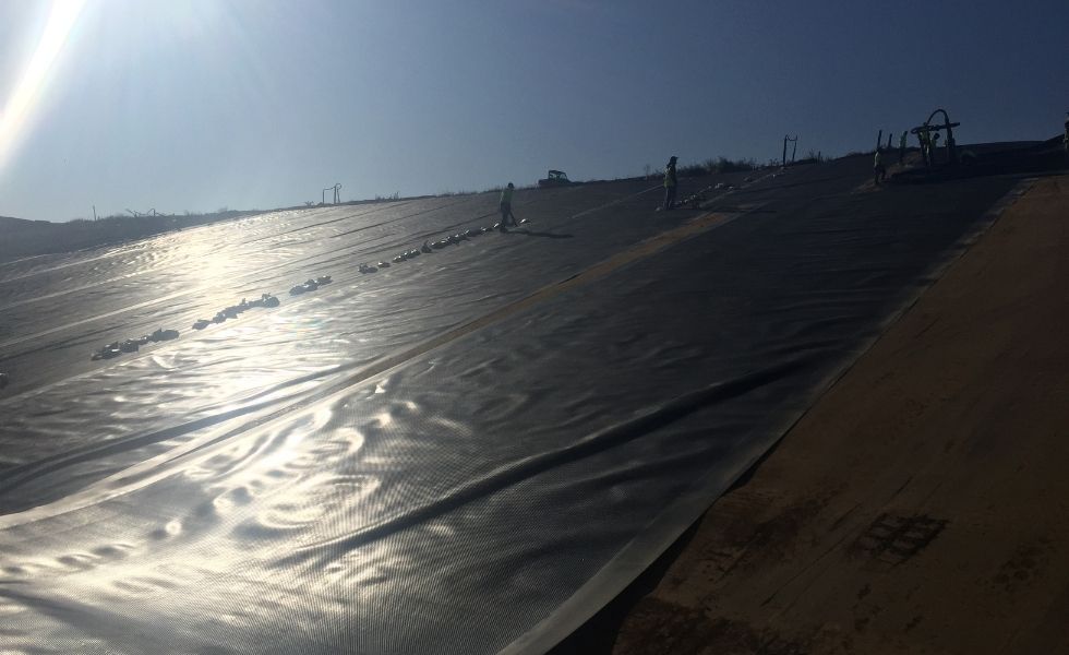 Workers installing a geomembrane liner across a large engineered slope at the PhilaPort Auto Storage Facility construction site.