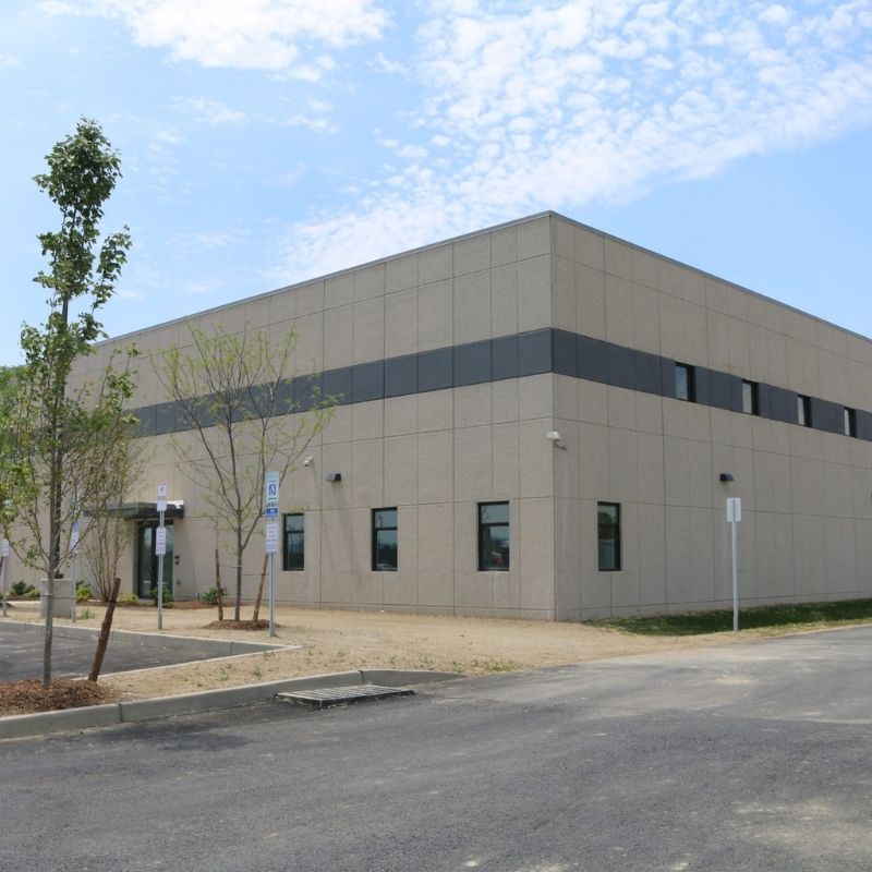 Exterior view of the PharmaCannis Medical Marijuana Facility in Hamptonburgh, New York, showing a modern industrial research and manufacturing building with concrete wall panels, landscaped grounds, and adjacent parking areas.