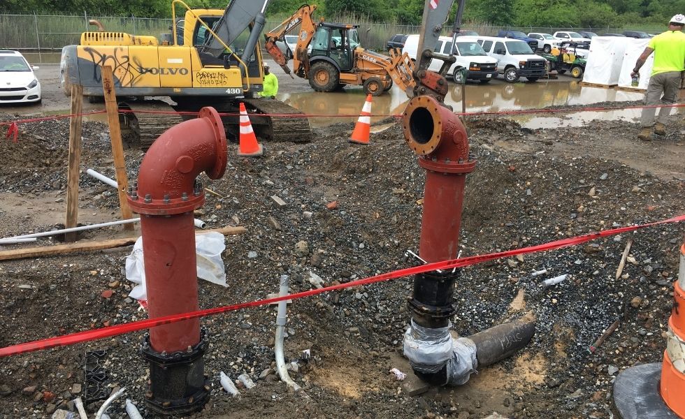 Red fire protection utility risers being installed at the Philaport Auto Facility construction site, with excavation equipment, traffic control devices.