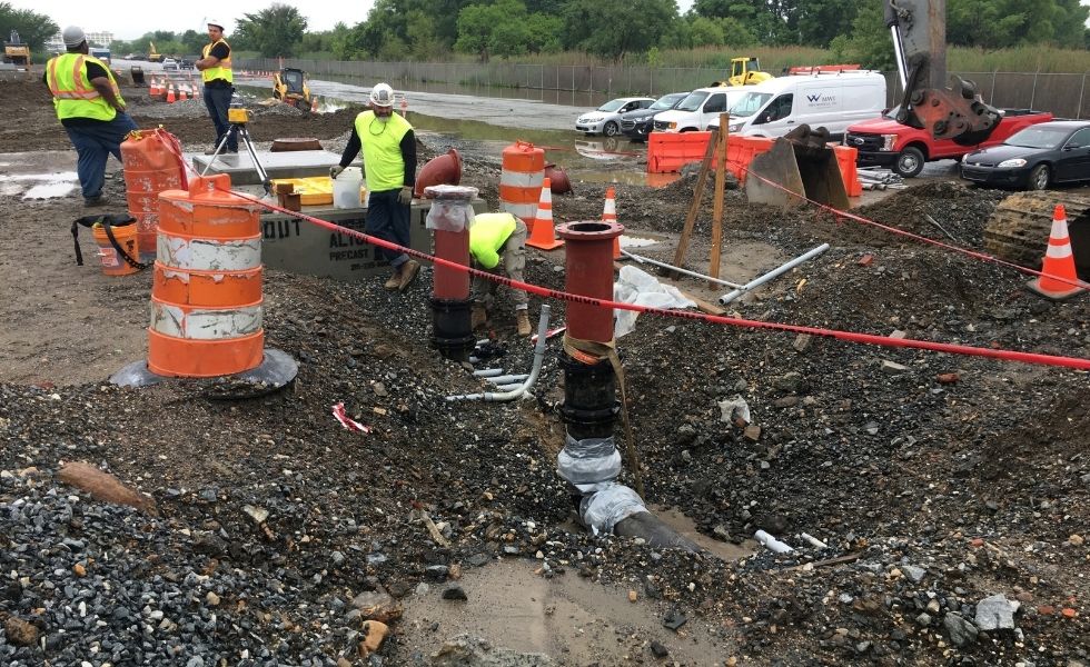 Workers installing fire water line infrastructure and vertical utility connections at the Philaport Auto Facility project site, surrounded by excavation activities, construction equipment