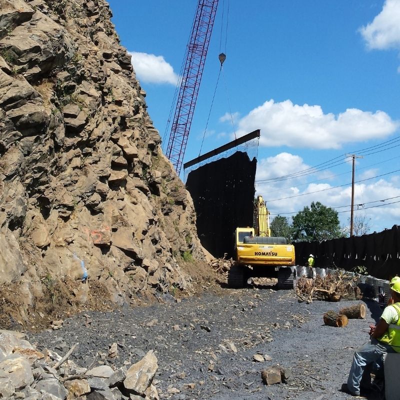 US 11/15 Rock Slope Safety Improvement, PA project: construction equipment and field personnel performing rock slope stabilization and rockfall mitigation activities along a steep roadway rock cut.