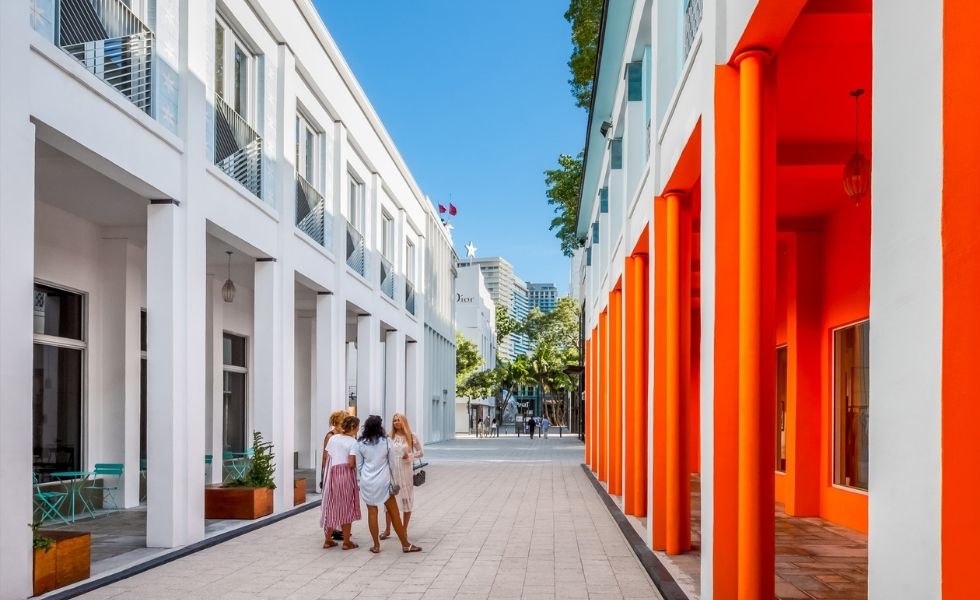 A pedestrian walkway in the Miami Design District bordered by modern white buildings and striking orange columns