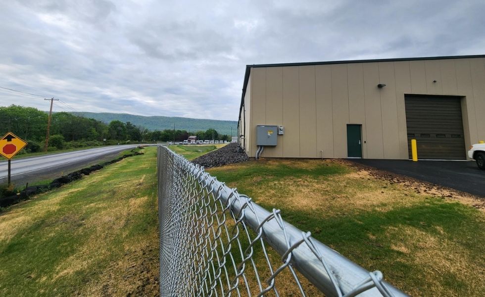 Side view of the STEP Williamsport Transportation Facility in Pennsylvania, featuring a maintenance building with a large overhead door, perimeter fencing, landscaped grounds