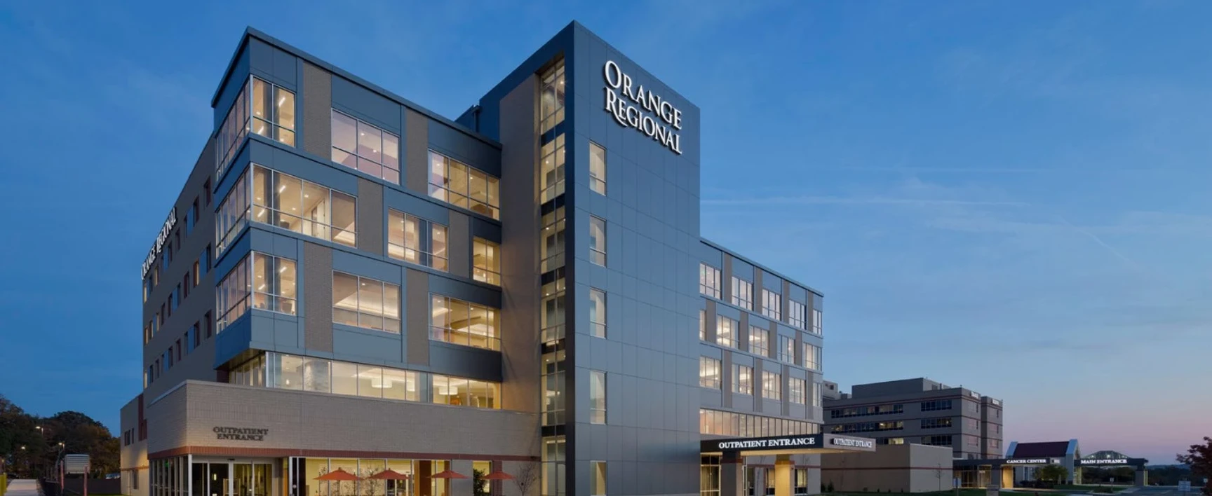 A multi‑story hospital building with large windows, photographed at dusk