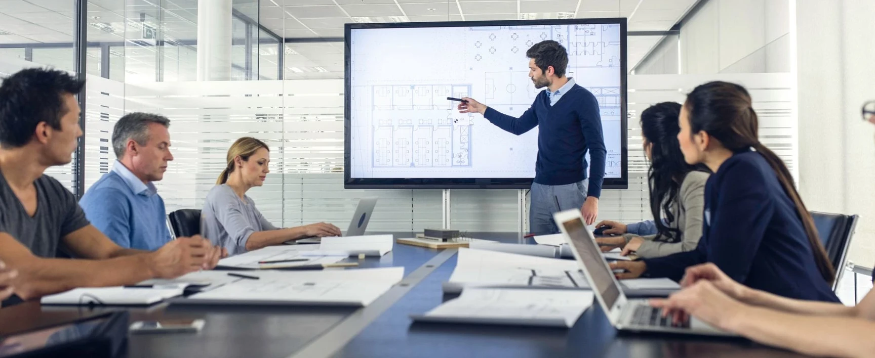 A presenter points to architectural floor plans on a screen during a professional training session