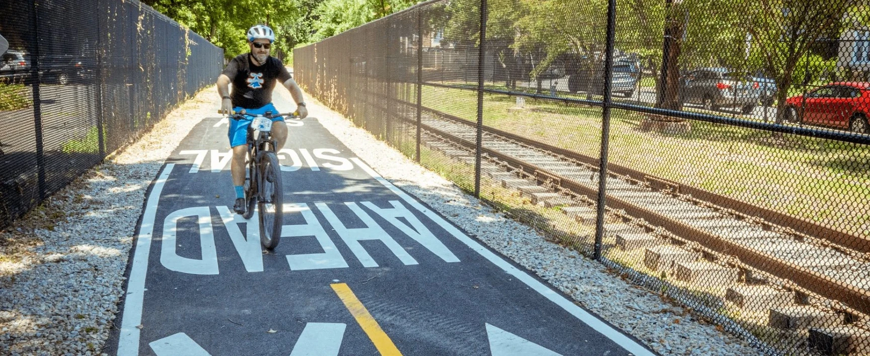 yclist using the Fox Chase Lorimer Trail as part of the Department of Streets On Call – GES project in Philadelphia, Pennsylvania, featuring a paved multi-use trail adjacent to railway tracks.