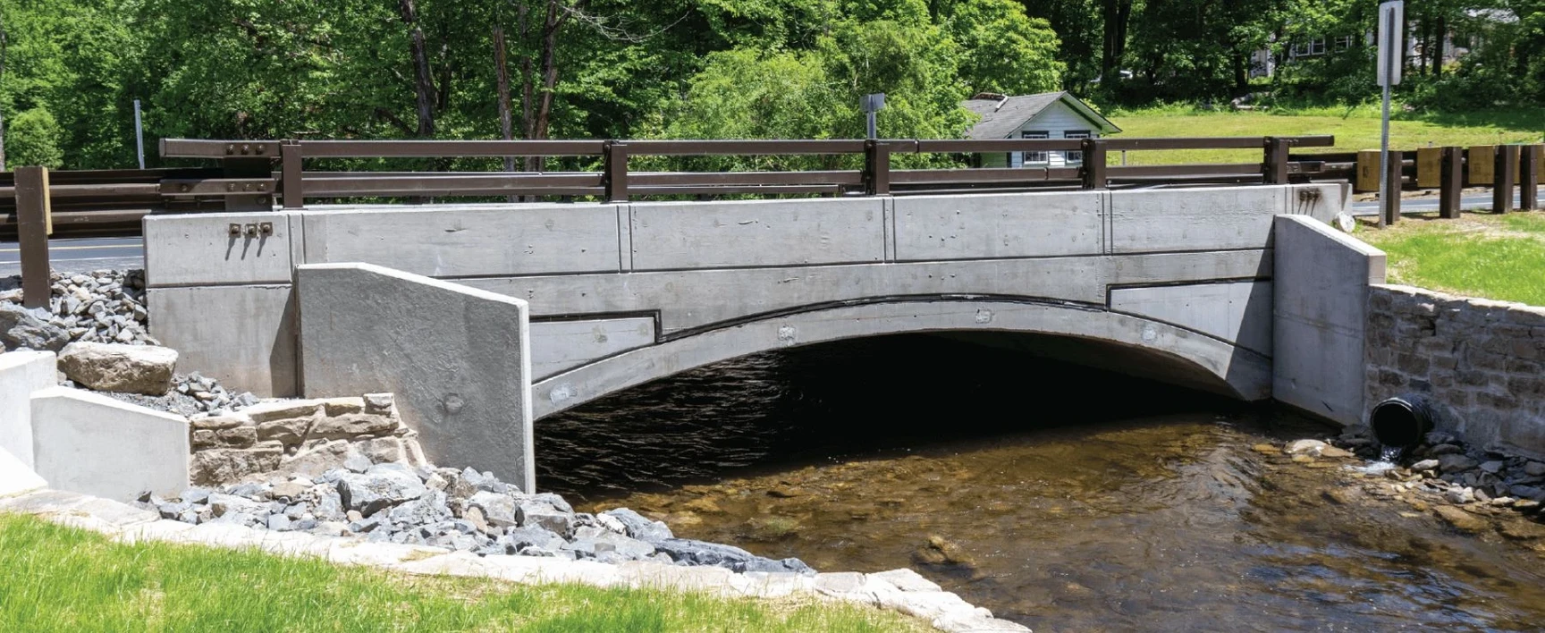 Completed McMichael’s Creek Bridge project in Pennsylvania, featuring a concrete arch bridge spanning a shallow stream, with roadway guardrails, stone riprap, and restored stream banks designed to improve transportation infrastructure and waterway resilience.