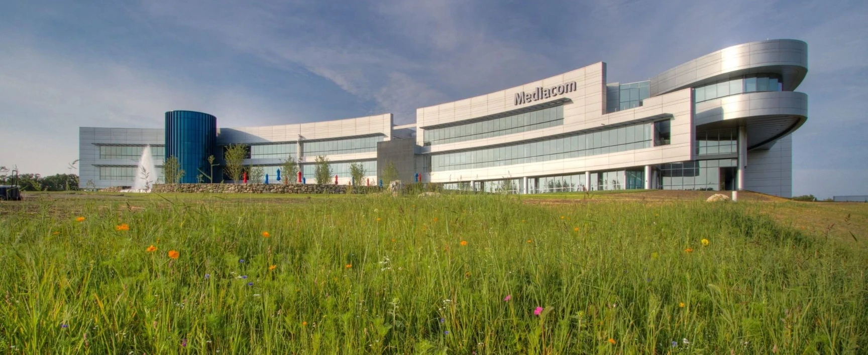 Mediacom Corporate Headquarters, NY: modern corporate office building with a curved architectural design, extensive glass façades, landscaped grounds, and open green space in the foreground.