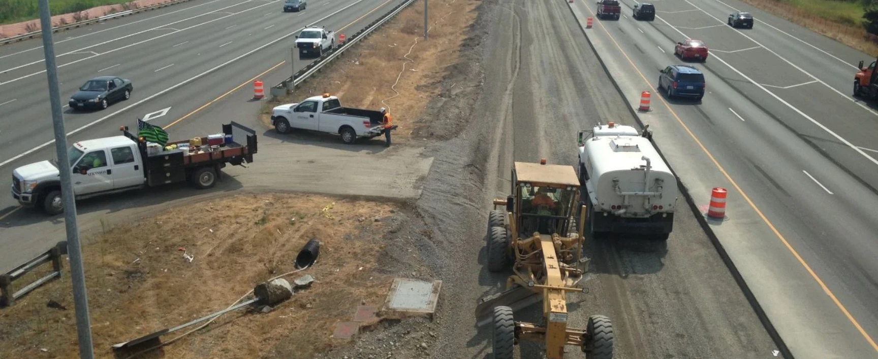 Construction equipment and work vehicles grading a new roadway section alongside active traffic lanes as part of the SR 167 Corridor Improvements Project.
