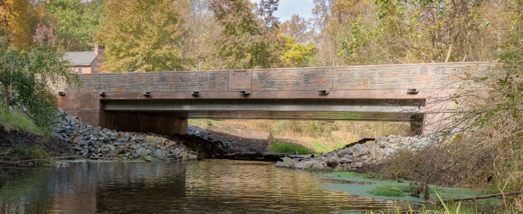 View of the Rapid Bridge Replacement Project, featuring a newly constructed bridge spanning a narrow waterway, with stone-faced abutments