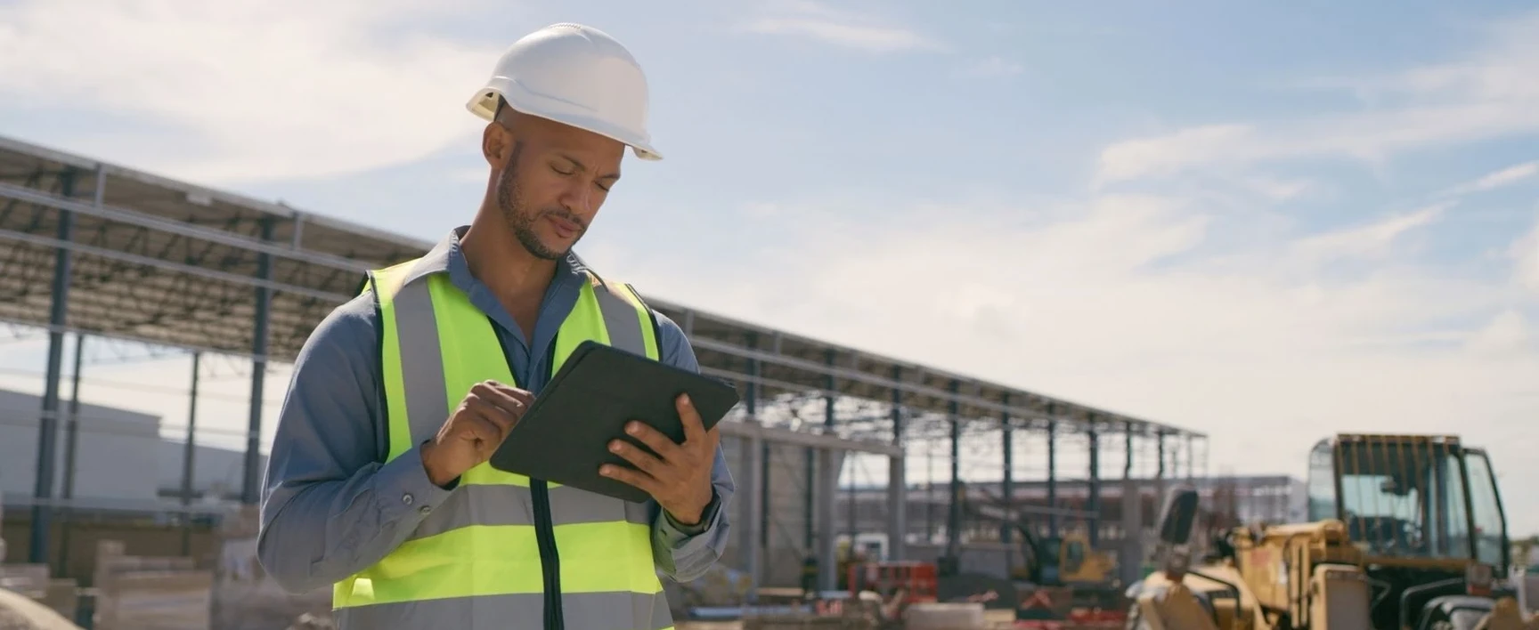 Construction inspector wearing safety equipment and using a tablet to document observations on an active construction site as part of special inspection