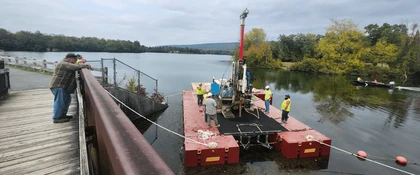 Memorial Lake Dam, PA: geotechnical investigation activities on a floating drilling platform near the dam, supporting dam safety assessment and infrastructure evaluation.